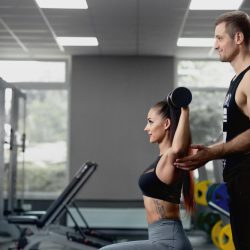 Antrenor personal care asistă o femeie în timpul unui exercițiu cu gantera