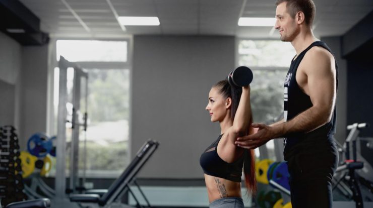Antrenor personal care asistă o femeie în timpul unui exercițiu cu gantera
